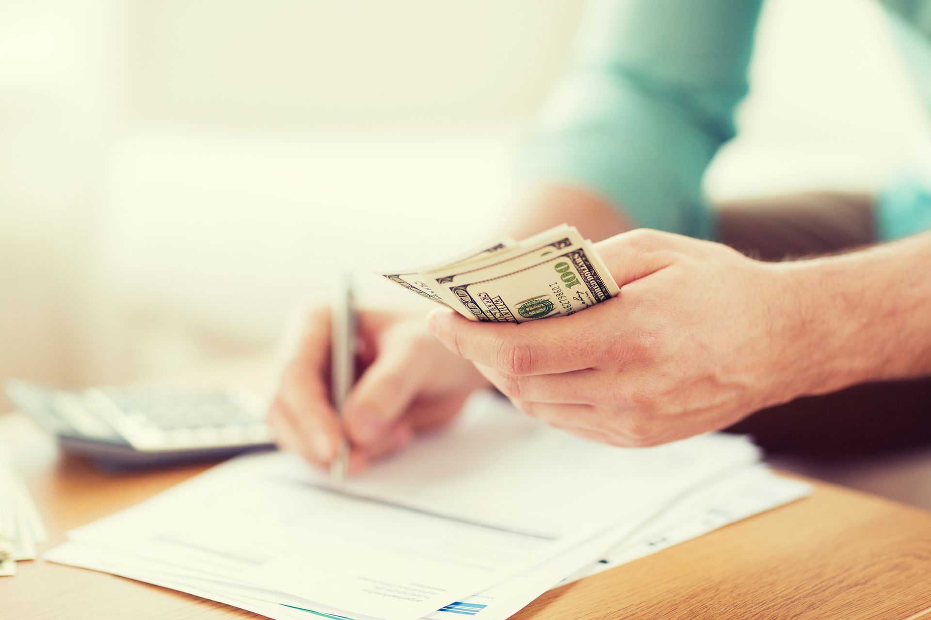 Person counting US dollar bills while writing on paper.