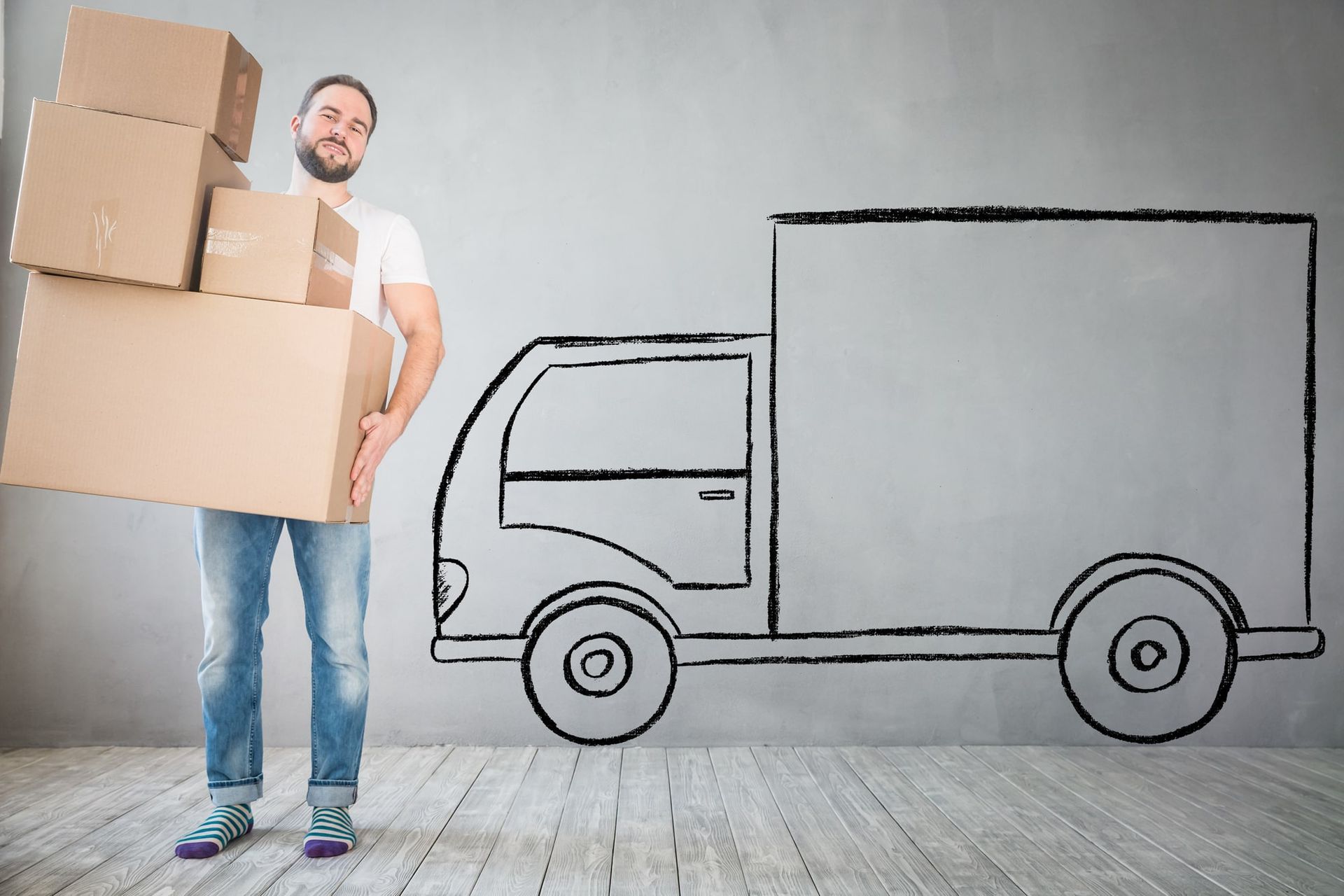 Man holding boxes, standing in front of a wall with a drawn truck, smiling.