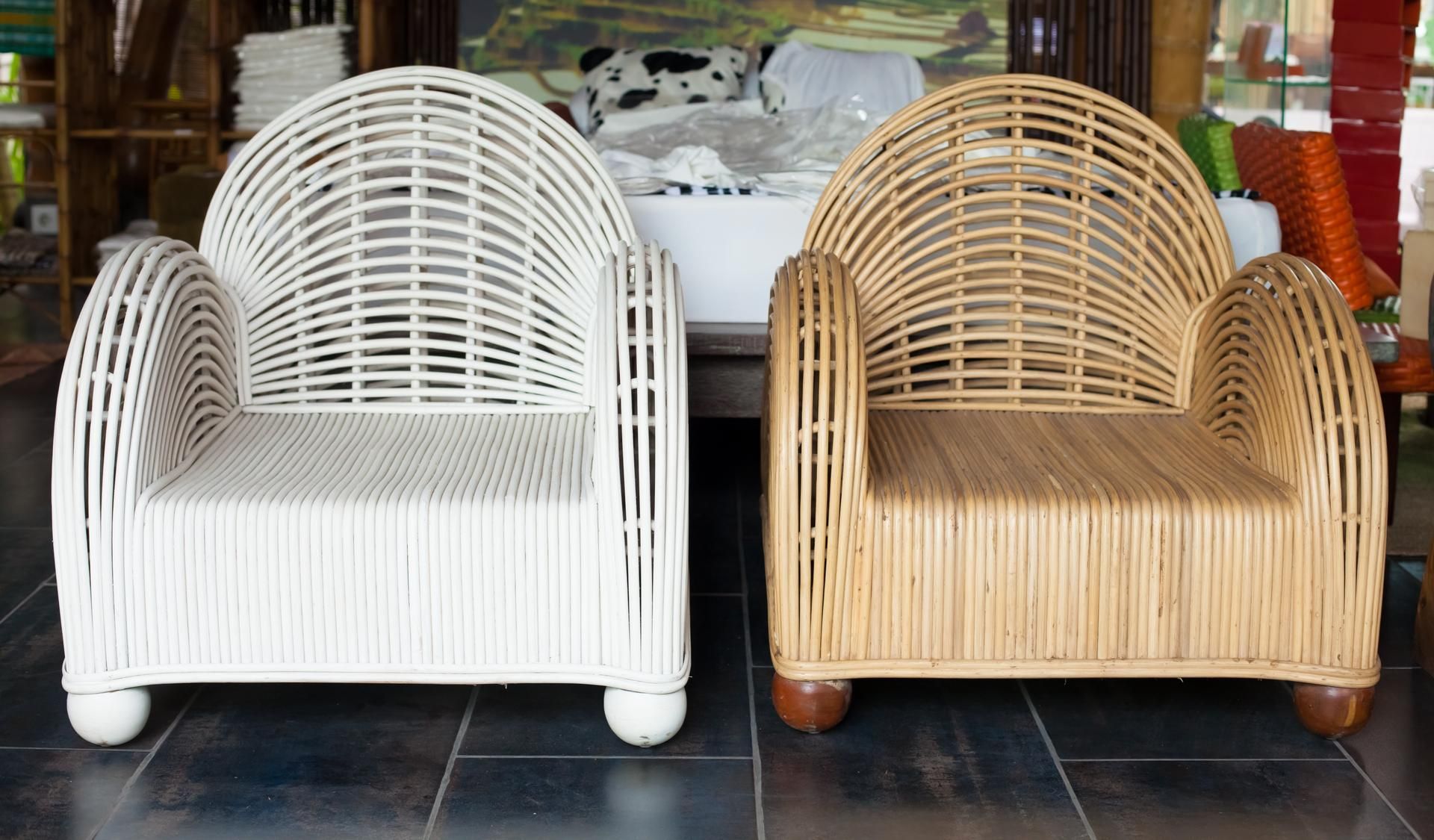 Two rattan armchairs, one white, one tan, side-by-side on a dark tiled floor.