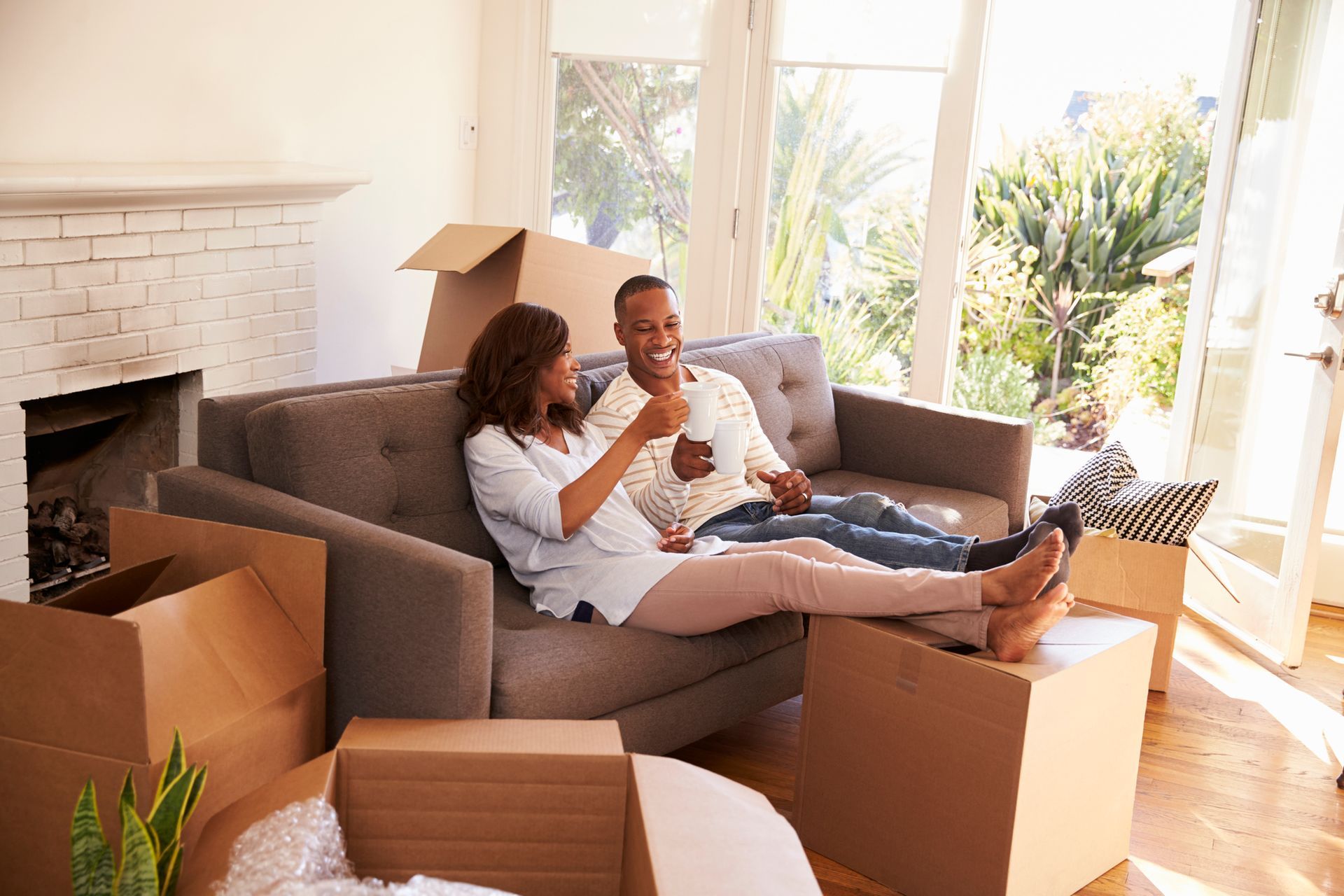 Couple relaxing on a couch in a new home, surrounded by moving boxes, smiling.