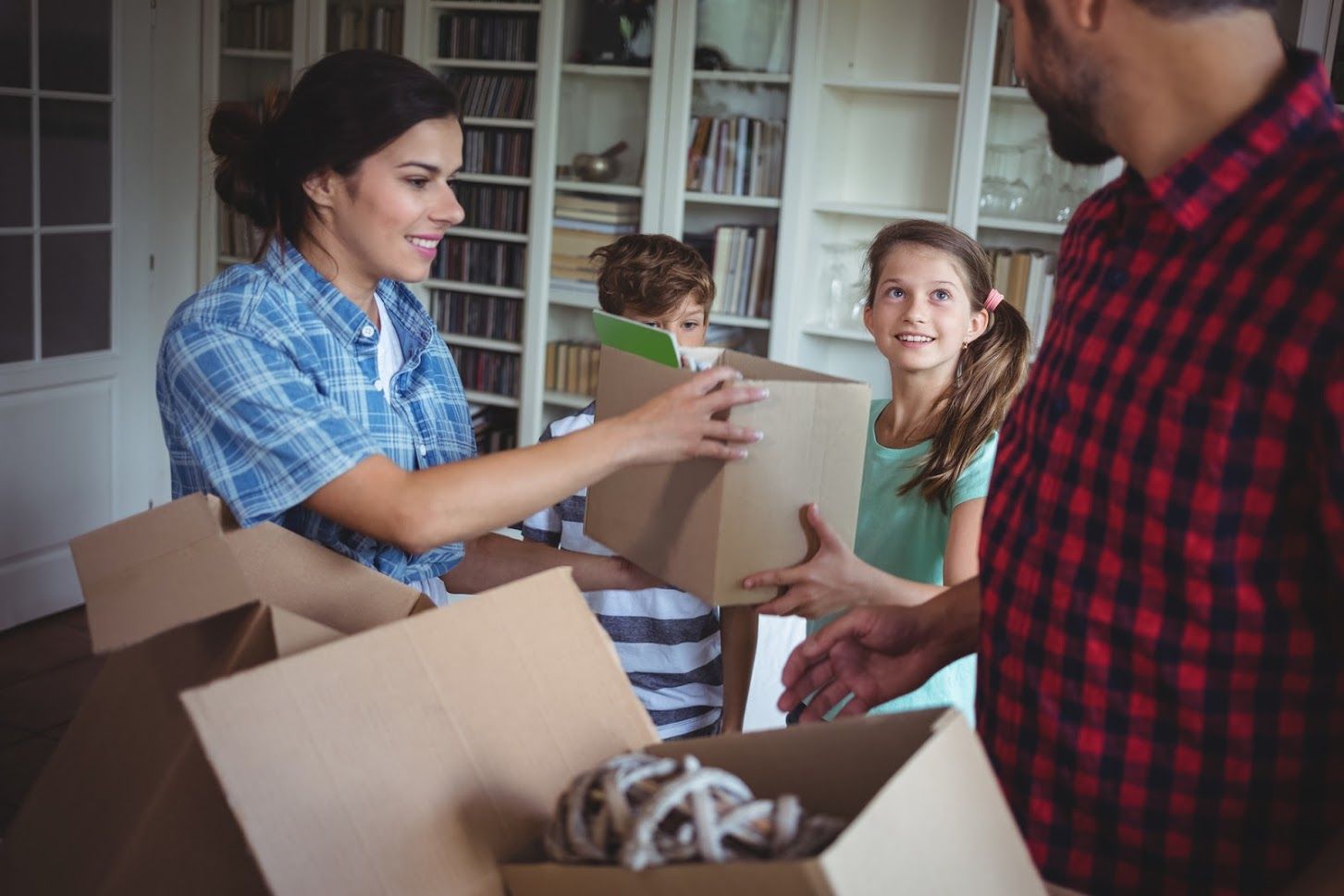 Family packing boxes, smiling, in front of bookshelves.