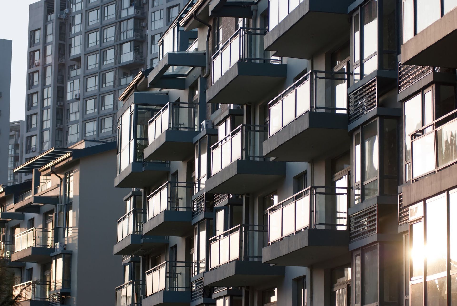 Apartment building with multiple balconies, some with sunlight reflecting off the glass.