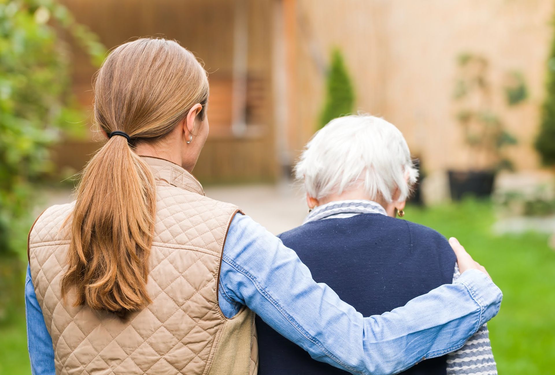 Young woman with arm around an elderly woman, walking together in a garden.