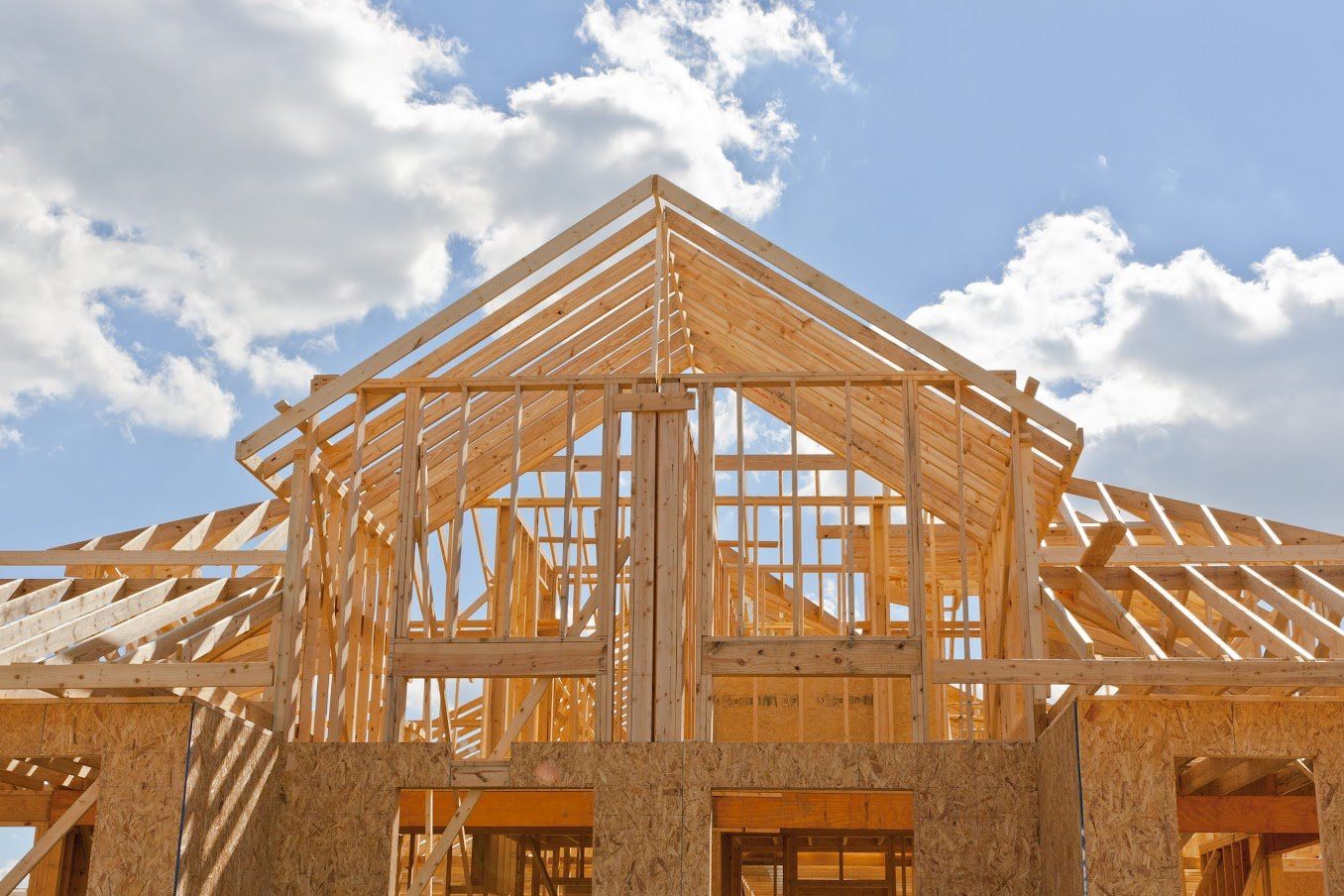 Wooden framework of a house under construction against a blue sky with clouds.