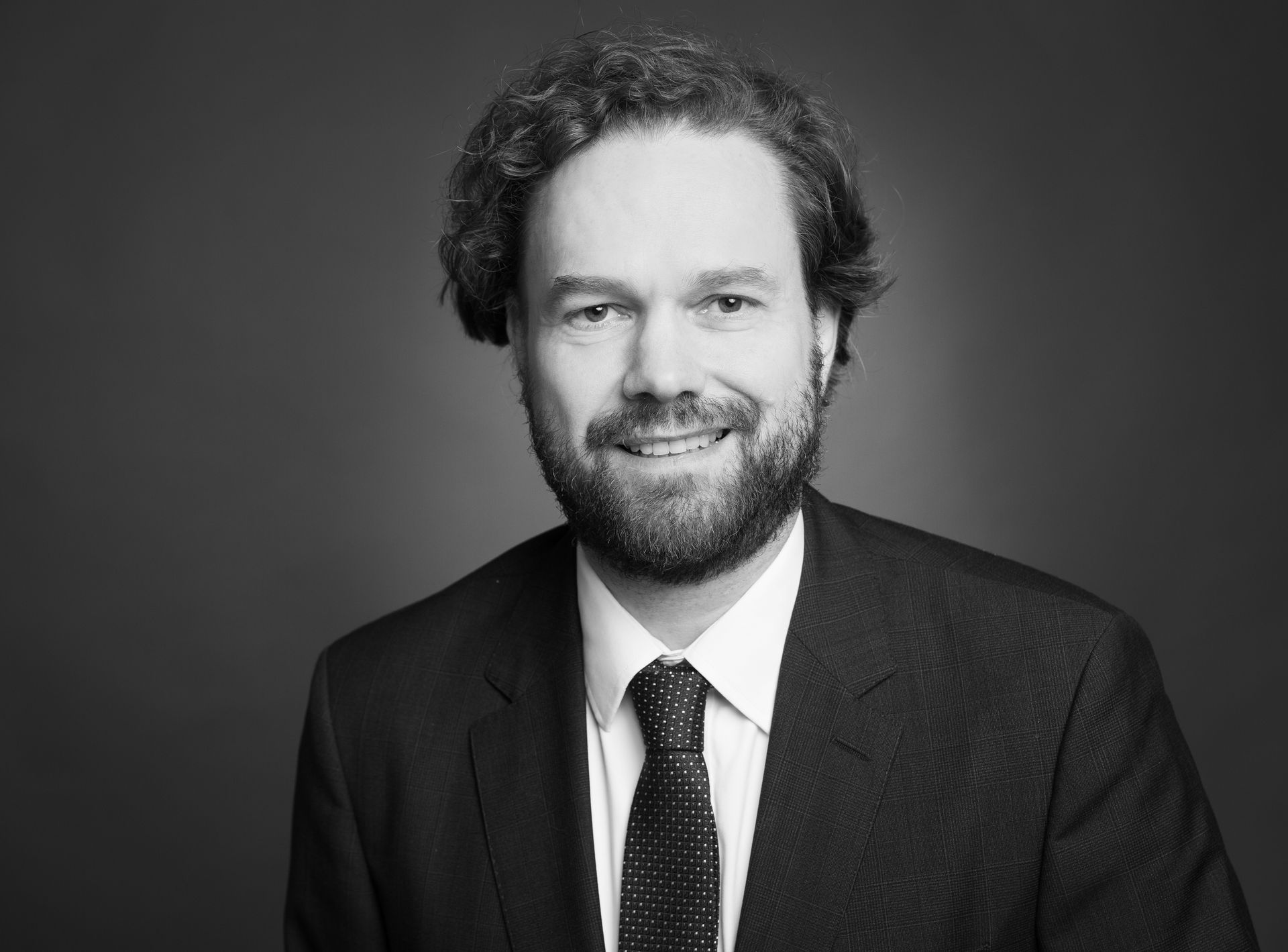 Auf einem Schwarzweißfoto lächelt ein Mann in Anzug und Krawatte.