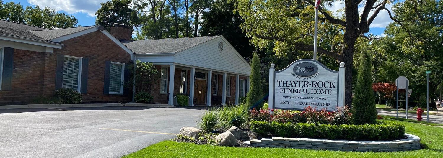 Front entrance of a brick building with a sign and landscaped flower bed under a blue sky
