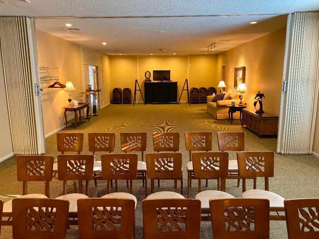 A room with chairs facing a screen and seating area. Beige walls, patterned carpet, and open dividers.