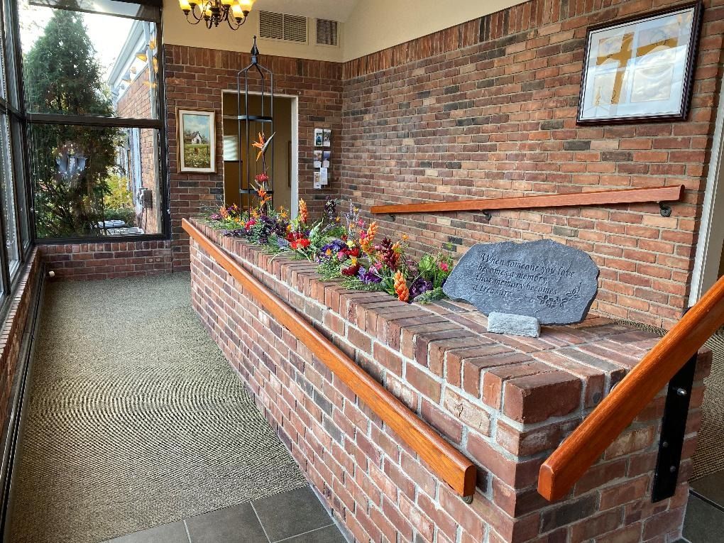Brick hallway with a built-in planter featuring flowers, a handrail, and a stone memorial.
