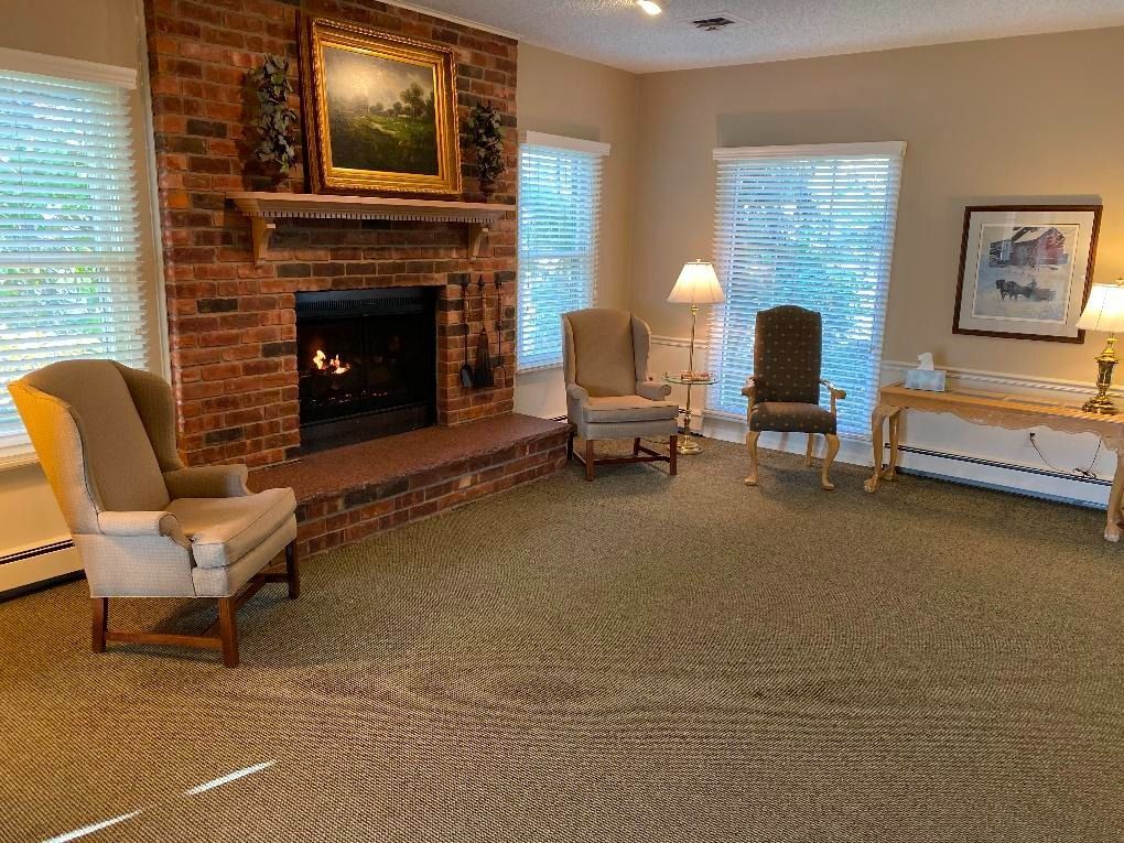 Living room with fireplace, chairs, and windows with blinds.