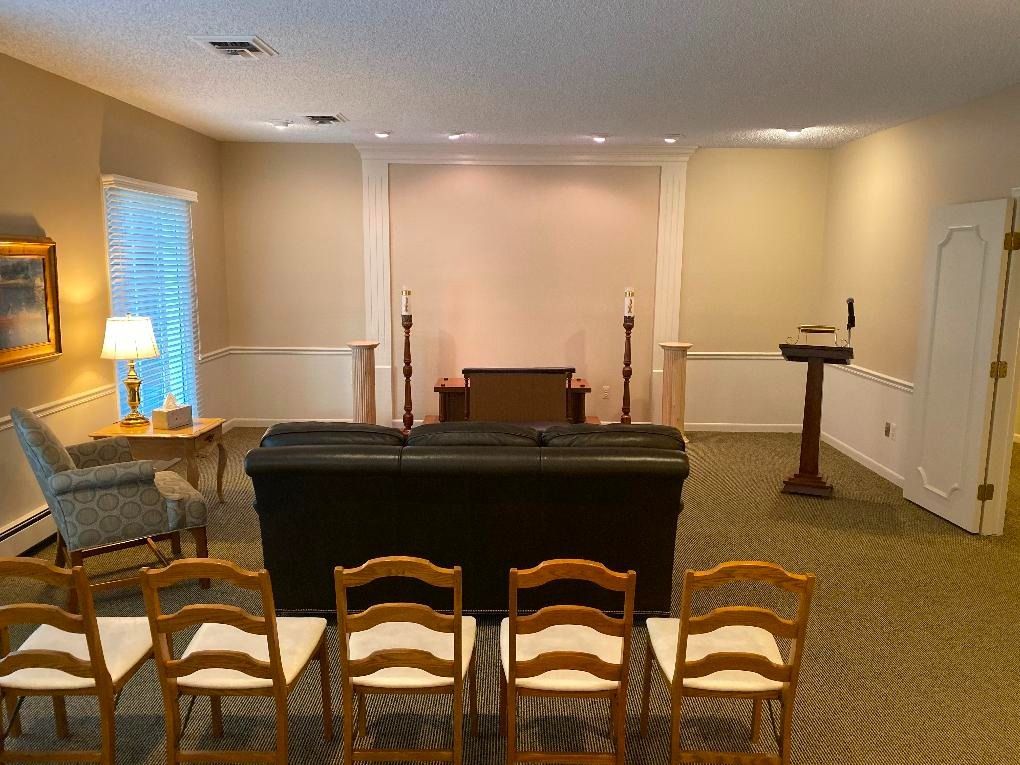 Interior of a funeral home chapel with chairs, casket, altar, and podium. Light colors dominate the room.