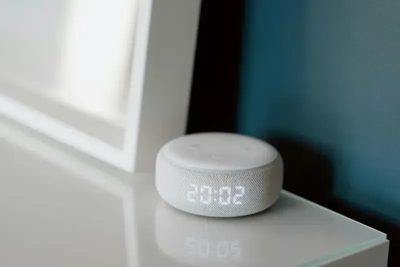A white clock is sitting on a table next to a mirror.