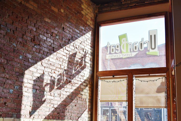 Sunlight on brick wall, window showing partial view of business logo; interior.