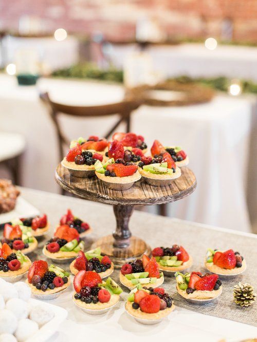 Fruit tarts on a wooden pedestal, arranged on a table with a white tablecloth in a bright setting.