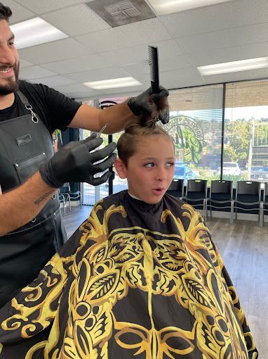 A young boy is getting his hair cut by a barber in a barber shop.