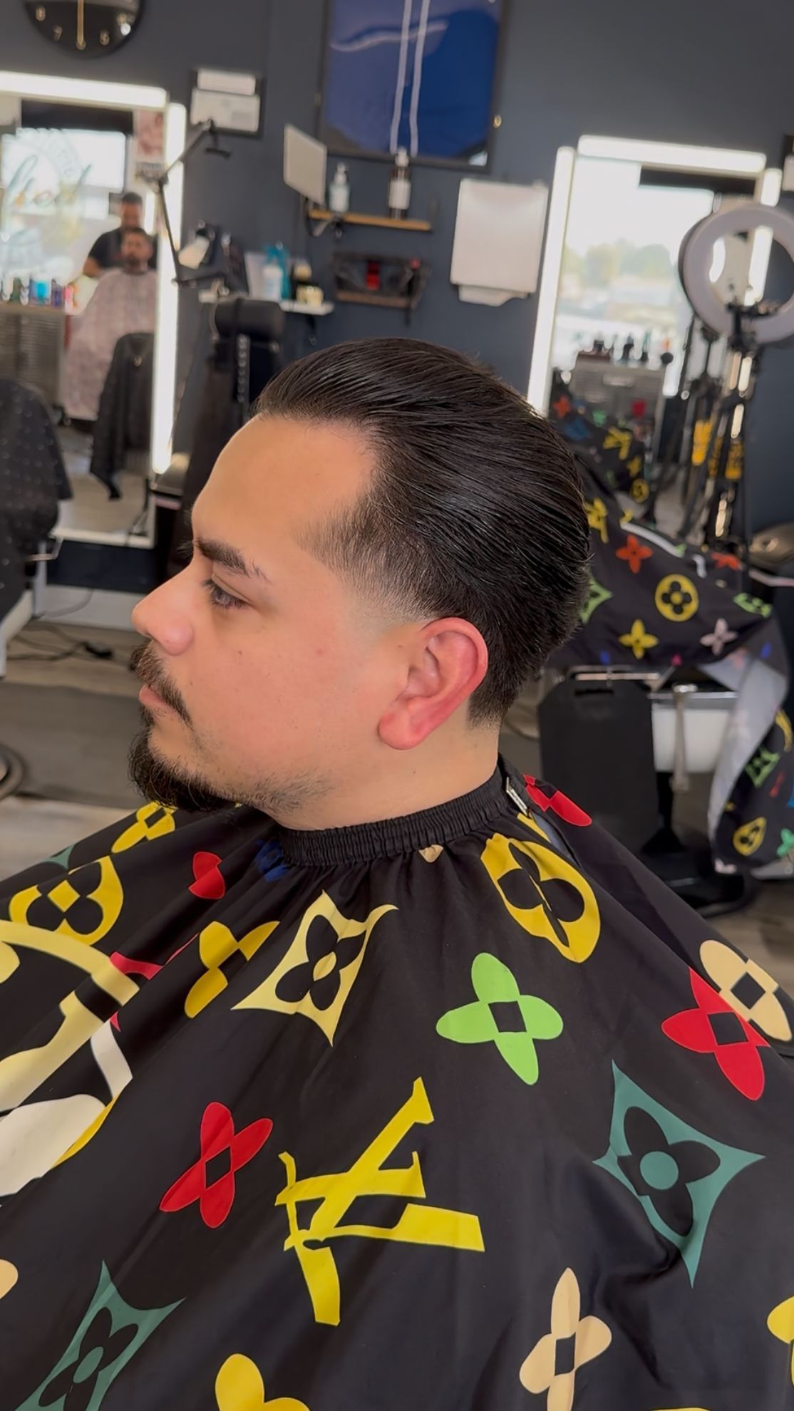 Man in barber chair getting a low fade haircut, wearing a Louis Vuitton cape.