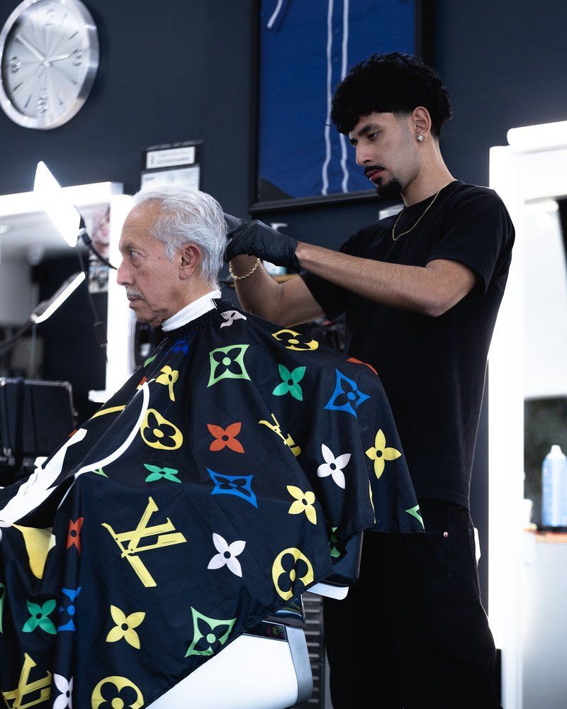 A man is getting his hair cut by a barber wearing a louis vuitton cape