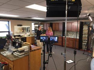 A man and a woman are standing in front of a camera in a kitchen.