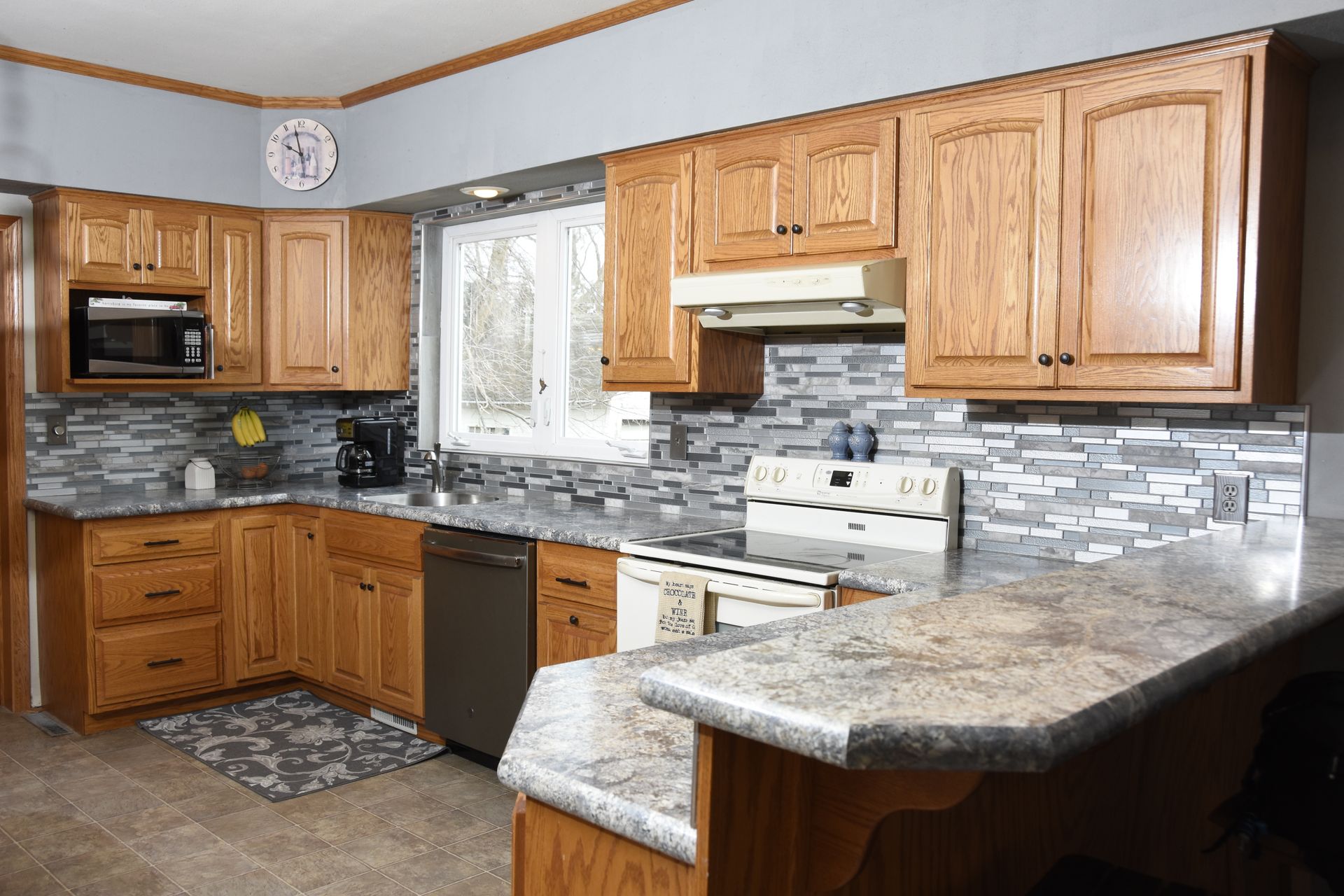 A kitchen with wooden cabinets , granite counter tops , stainless steel appliances and a clock on the wall.