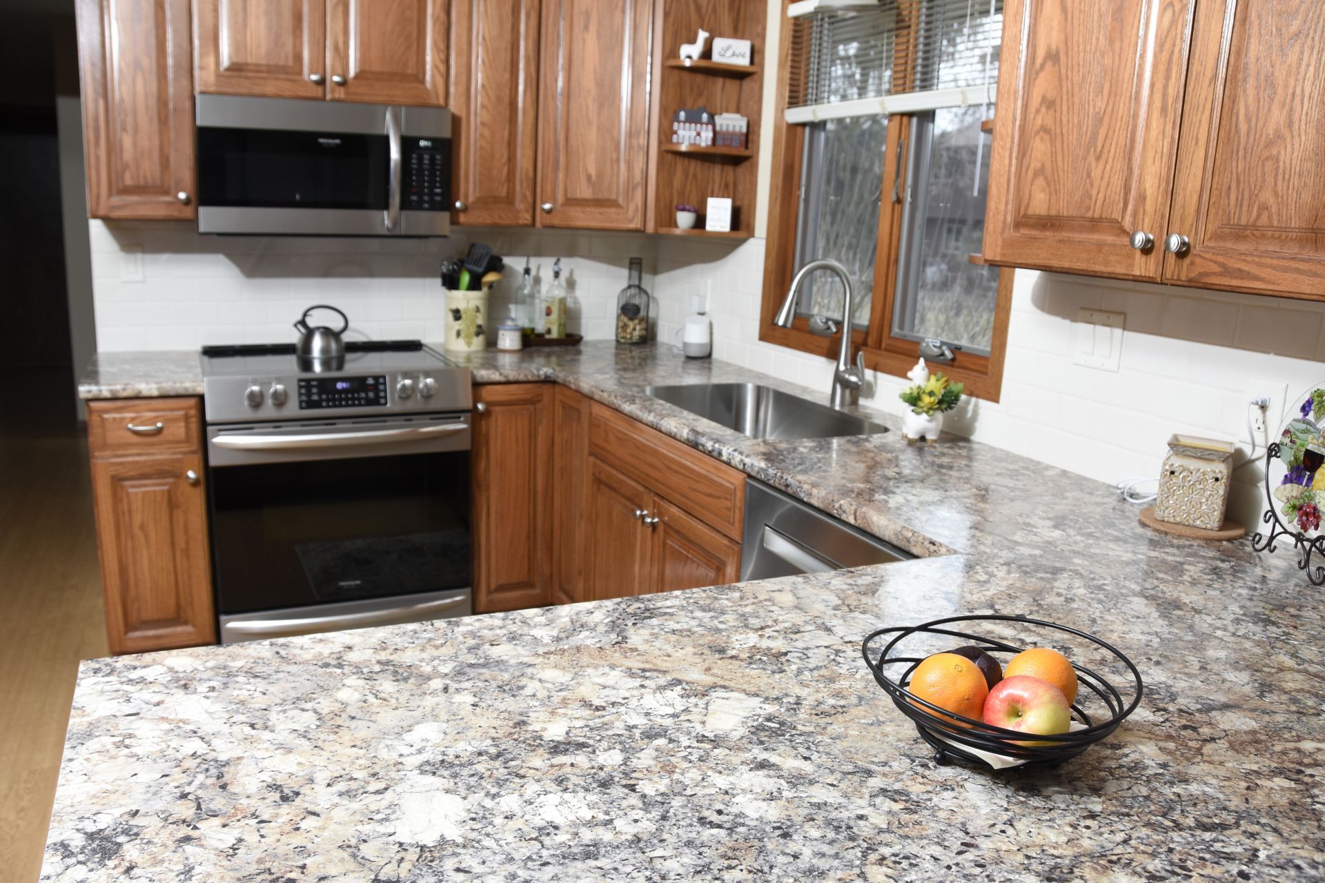 A kitchen with granite counter tops , wooden cabinets , stainless steel appliances and a bowl of fruit on the counter.