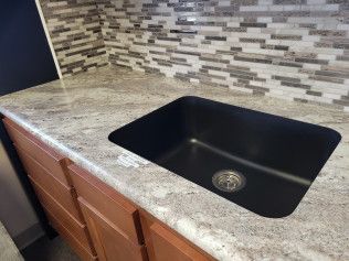 A black sink is sitting on top of a granite counter in a kitchen.