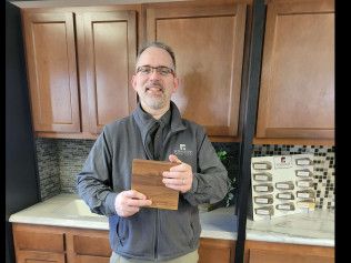 A man is holding a piece of wood in front of a kitchen counter.