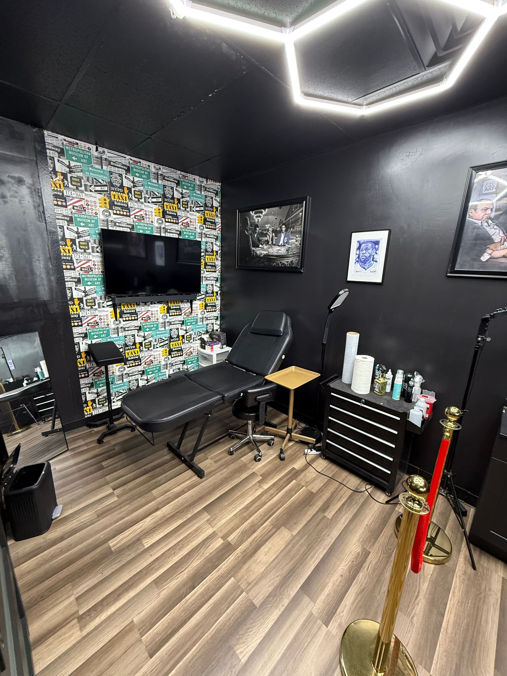 Tattoo studio interior with tattoo bed, graffiti wall, black walls, and overhead lighting.
