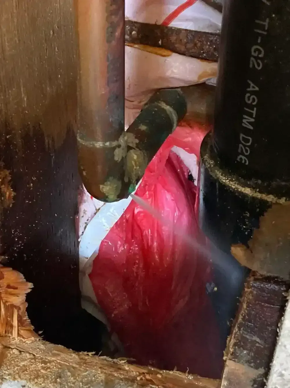 Copper and black pipes with a red plastic bag in a wall cavity, possibly a leak.