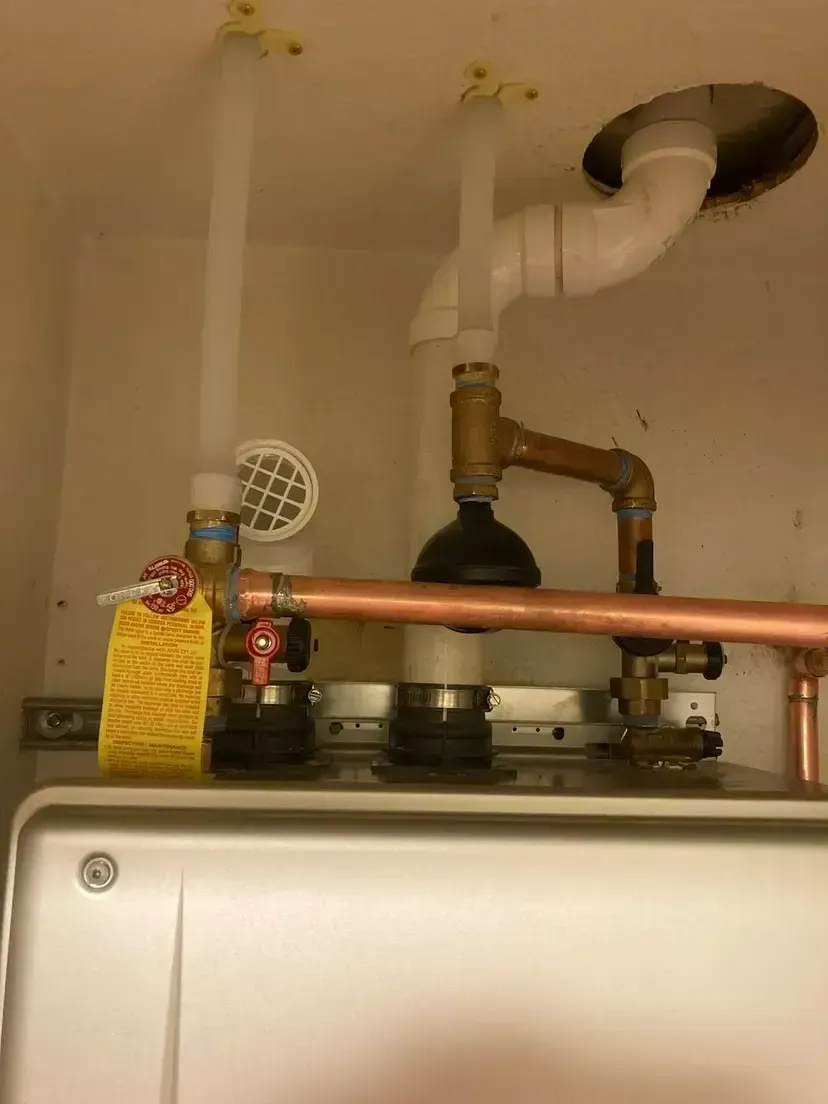 A gas boiler with white pipes and copper plumbing against a white wall.