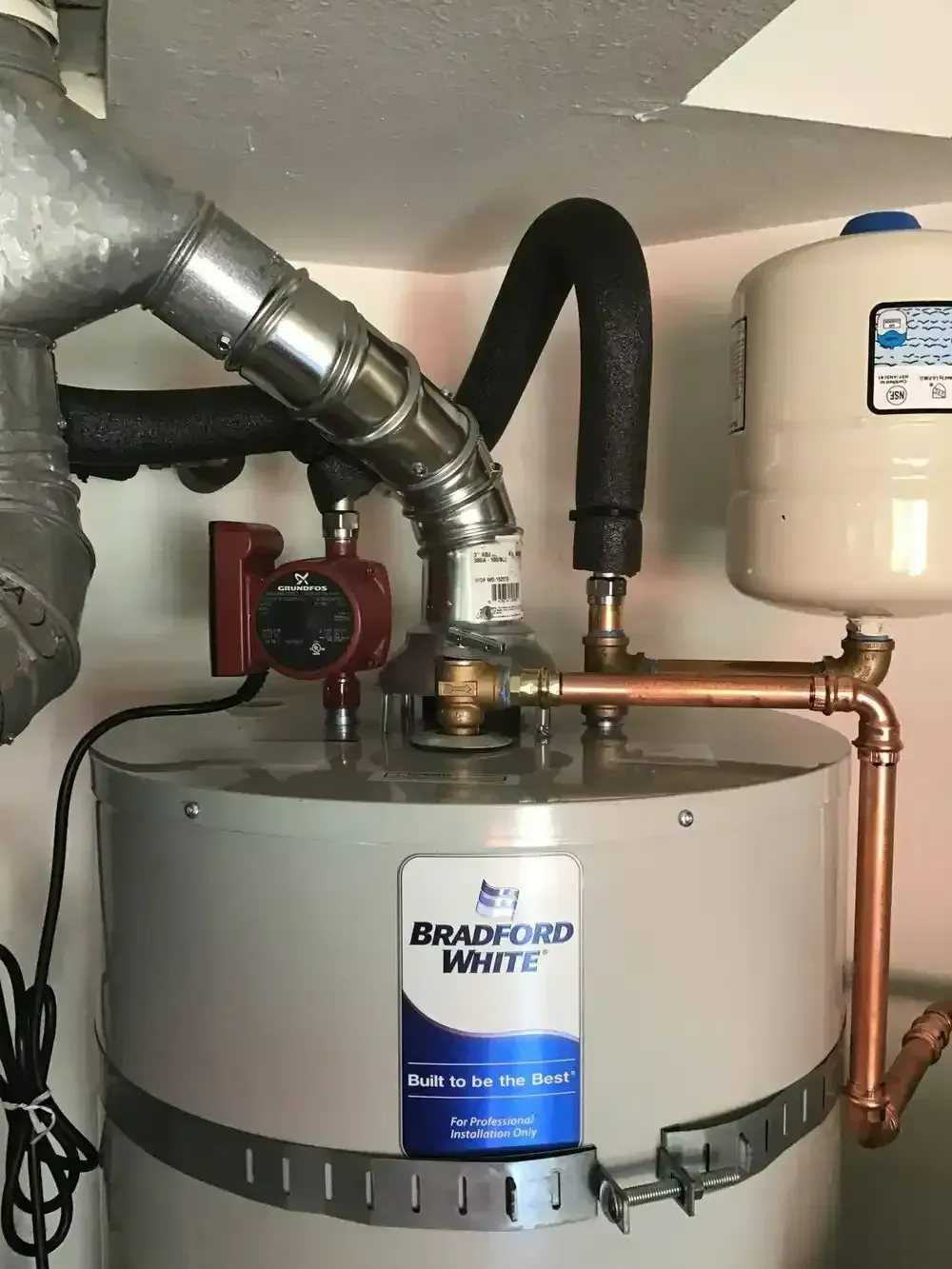 Water heater with copper pipes, a pump, and expansion tank in a corner.
