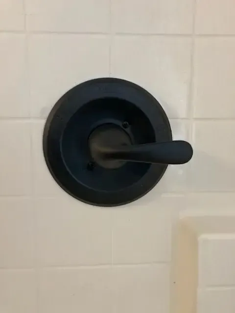 Black shower faucet on white tiled wall.