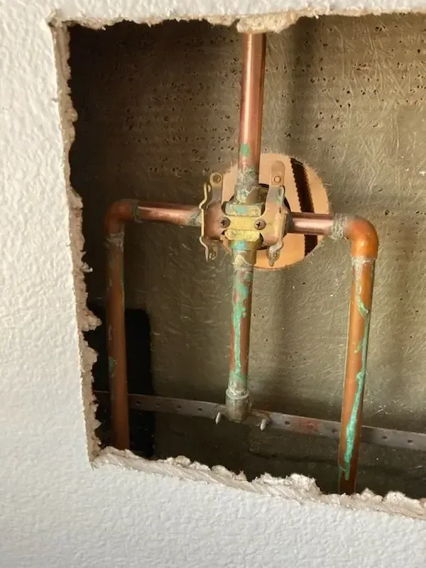 Copper plumbing fixtures in a wall cavity, with green oxidation visible.