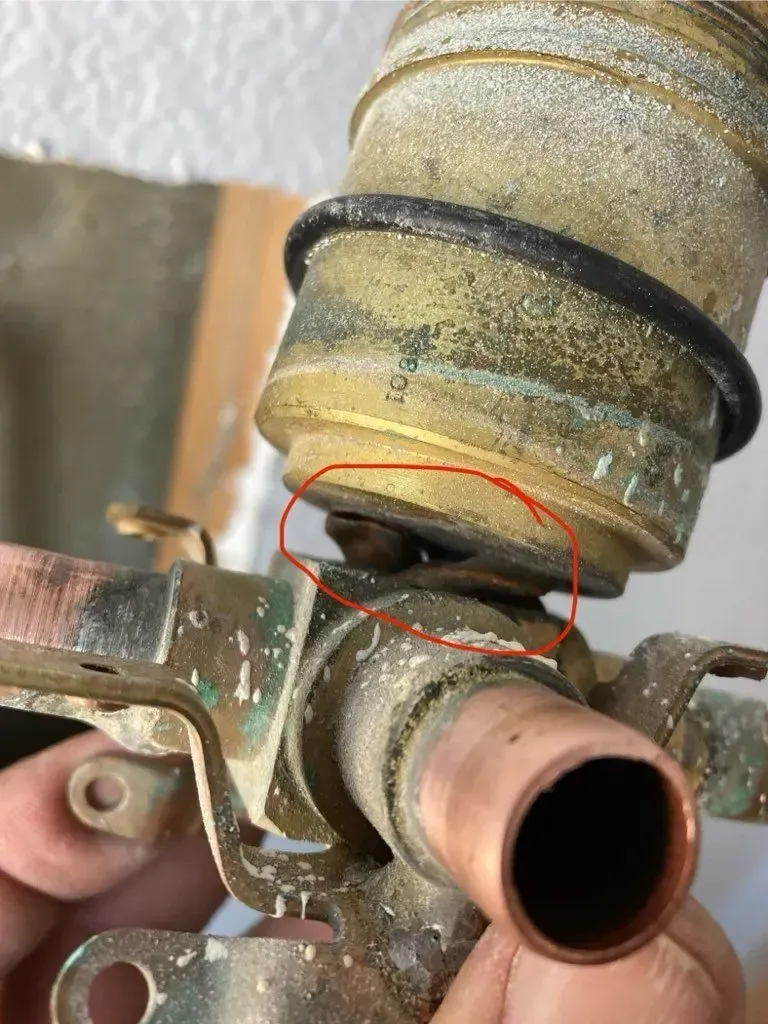 Close-up of a corroded brass plumbing fixture with a red circle highlighting a possible leak point.