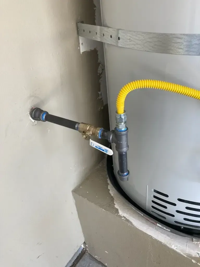 Gas water heater connection with black pipe and yellow flexible gas line.