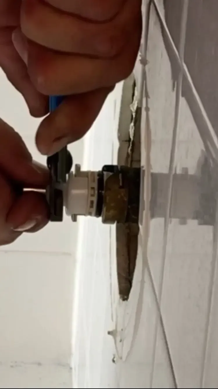 Hands using pliers to turn a white valve on a water fixture mounted in a white panel.