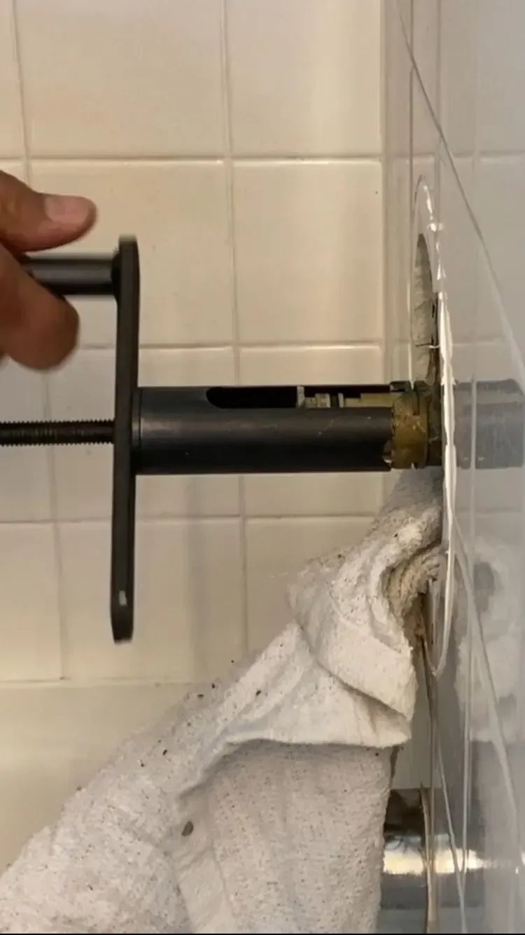 Person uses a tool to remove a shower valve stem from a tiled wall.