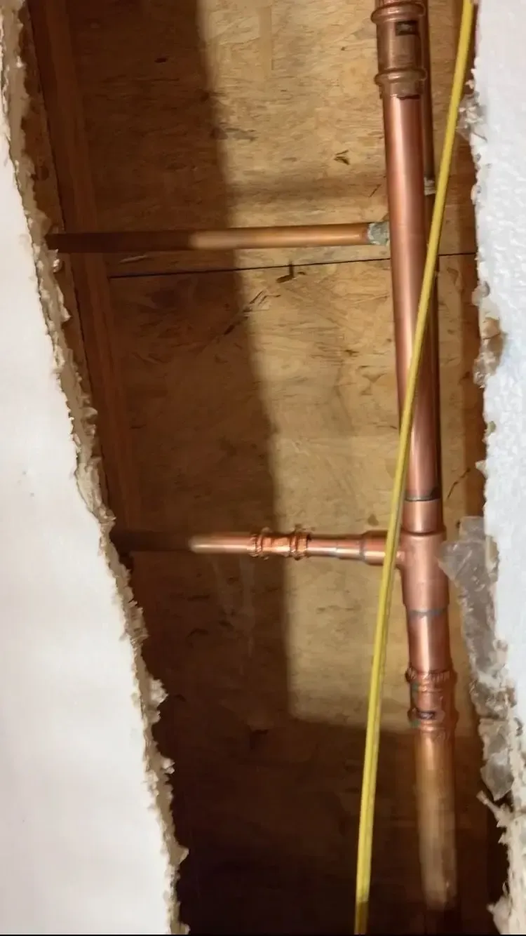 Copper pipes and fittings within a wall cavity, with a yellow wire running alongside.