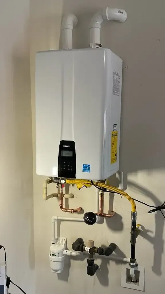 White tankless water heater mounted on a wall with gas and water lines.