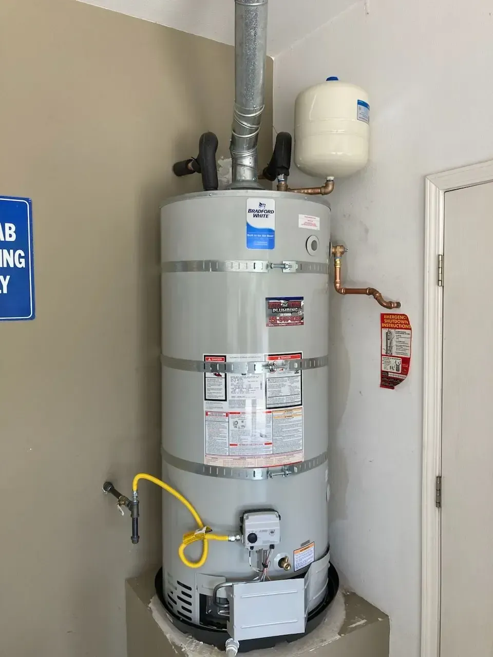 A tall, gray water heater with a vent pipe, expansion tank, and gas line, installed on a concrete base.