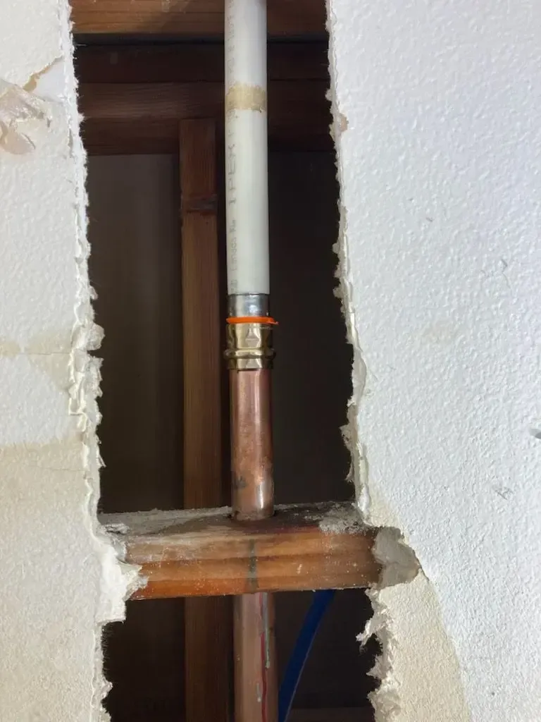 Plumbing repair: copper pipe connected to white plastic pipe within a wall cavity, orange rubber ring visible.