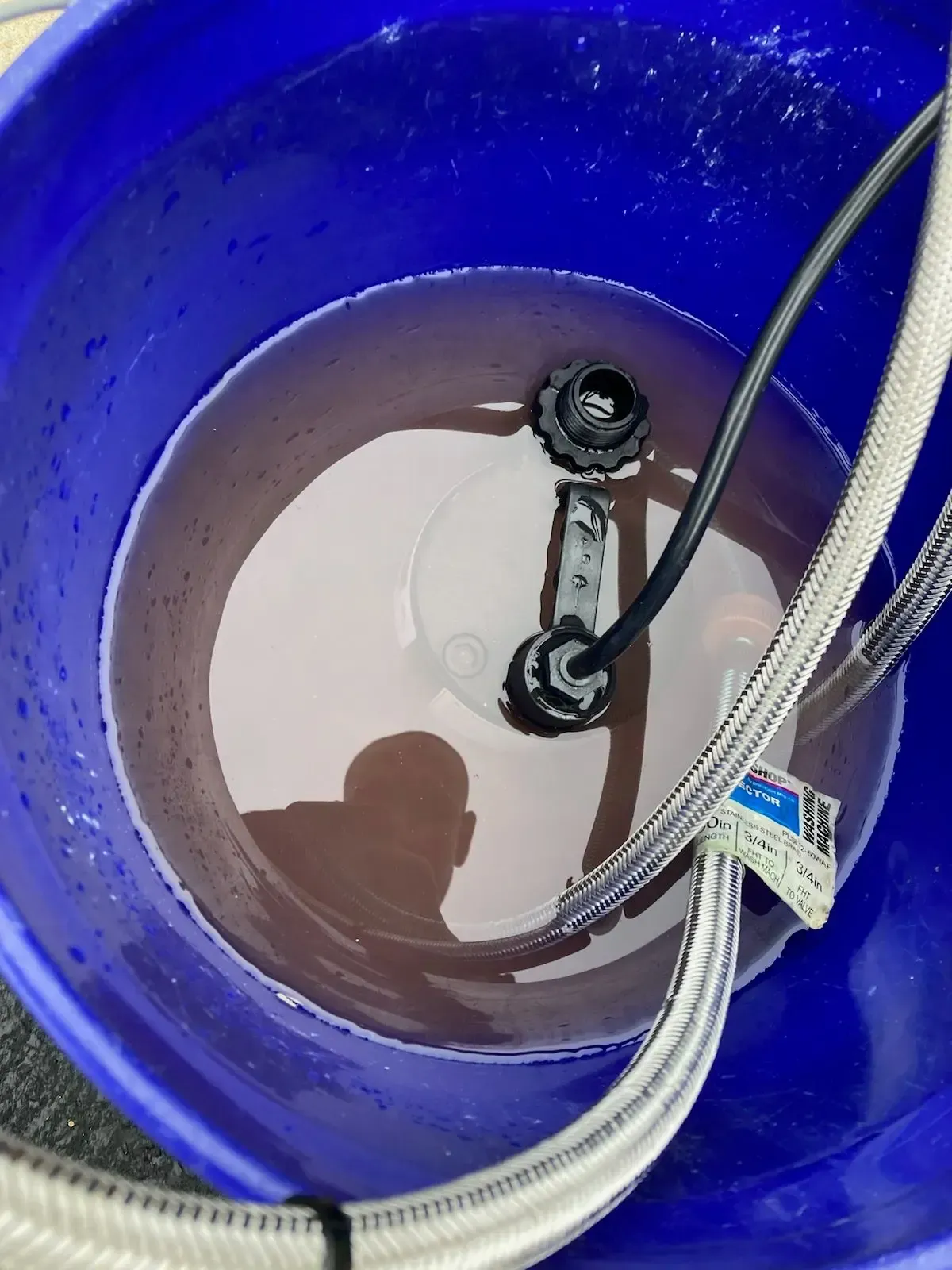 Blue bucket filled with reddish-brown water, submersible pump, and silver hose inside.