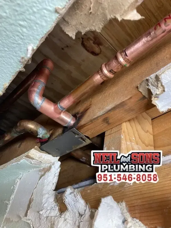 Copper plumbing pipes within a damaged wall; water stain and repair needed, Neilsons Plumbing phone number visible.