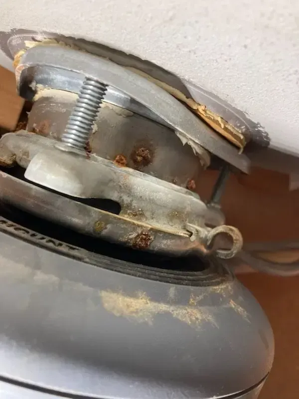 Corroded garbage disposal assembly beneath a kitchen sink. Metal parts are rusty, a coiled spring is visible.