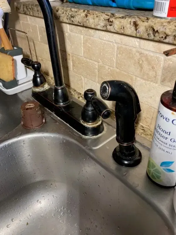 Black kitchen faucet with sprayer on a stainless steel sink; beige backsplash.