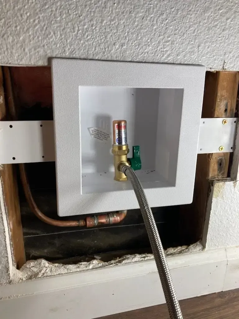 A laundry machine water supply box with copper pipes, a valve, and a silver braided hose.