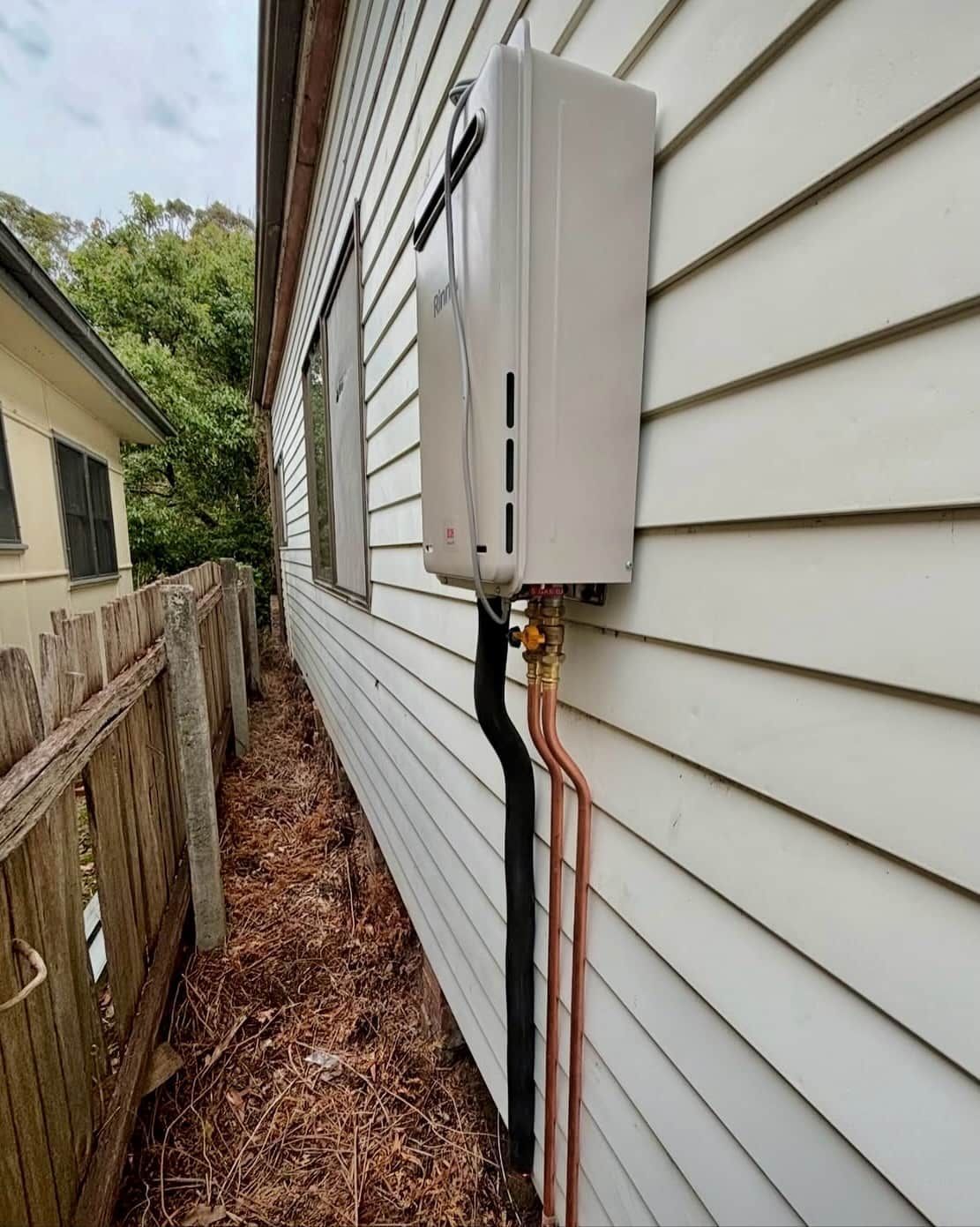 Outdoor utility meter box on white siding with exposed pipes along a house wall — Crystal Clear Plumbing & Roofing in Wollongong, NSW