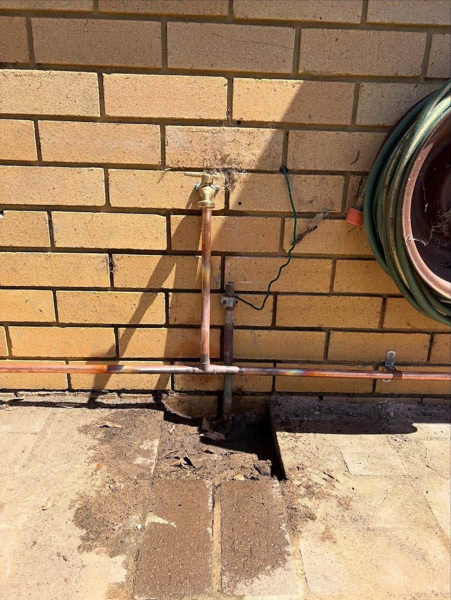 A Copper Plumbing Pipe Assembly Attached to a Brick Wall — Crystal Clear Plumbing & Roofing in Fairy Meadow, NSW