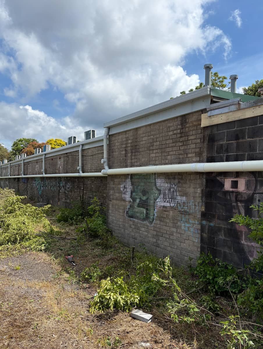 A Long Brick Wall With a White Pipe Running Horizontally — Crystal Clear Plumbing & Roofing in Fairy Meadow, NSW