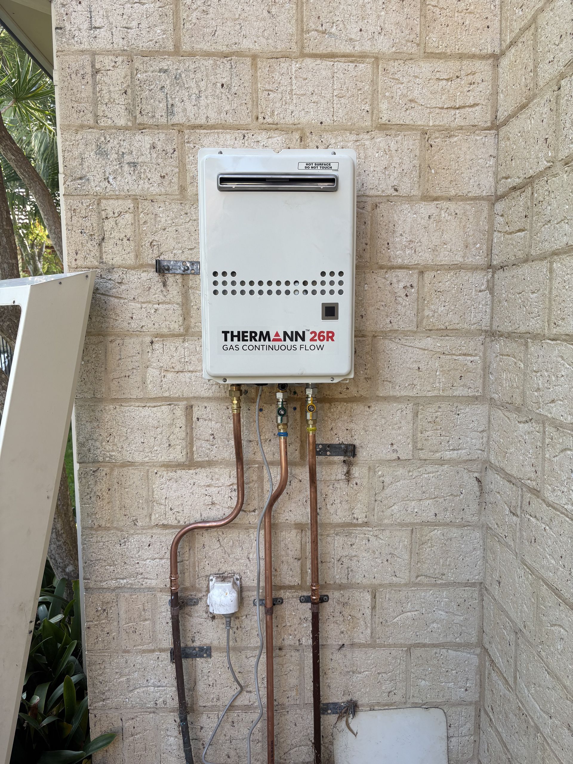 Wall-mounted gas water heater with exposed pipes on a stone exterior wall — Crystal Clear Plumbing & Roofing in Wollongong, NSW