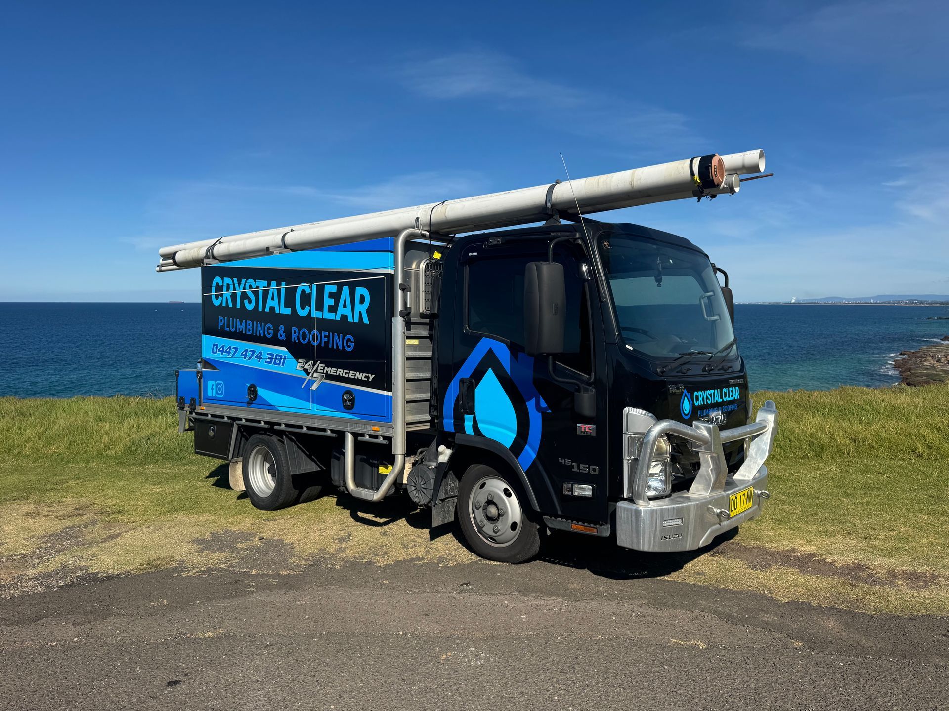 Blue Crystal Clear truck parked by the sea on grassy ground, with a ladder mounted on top — Crystal Clear Plumbing & Roofing in Wollongong, NSW