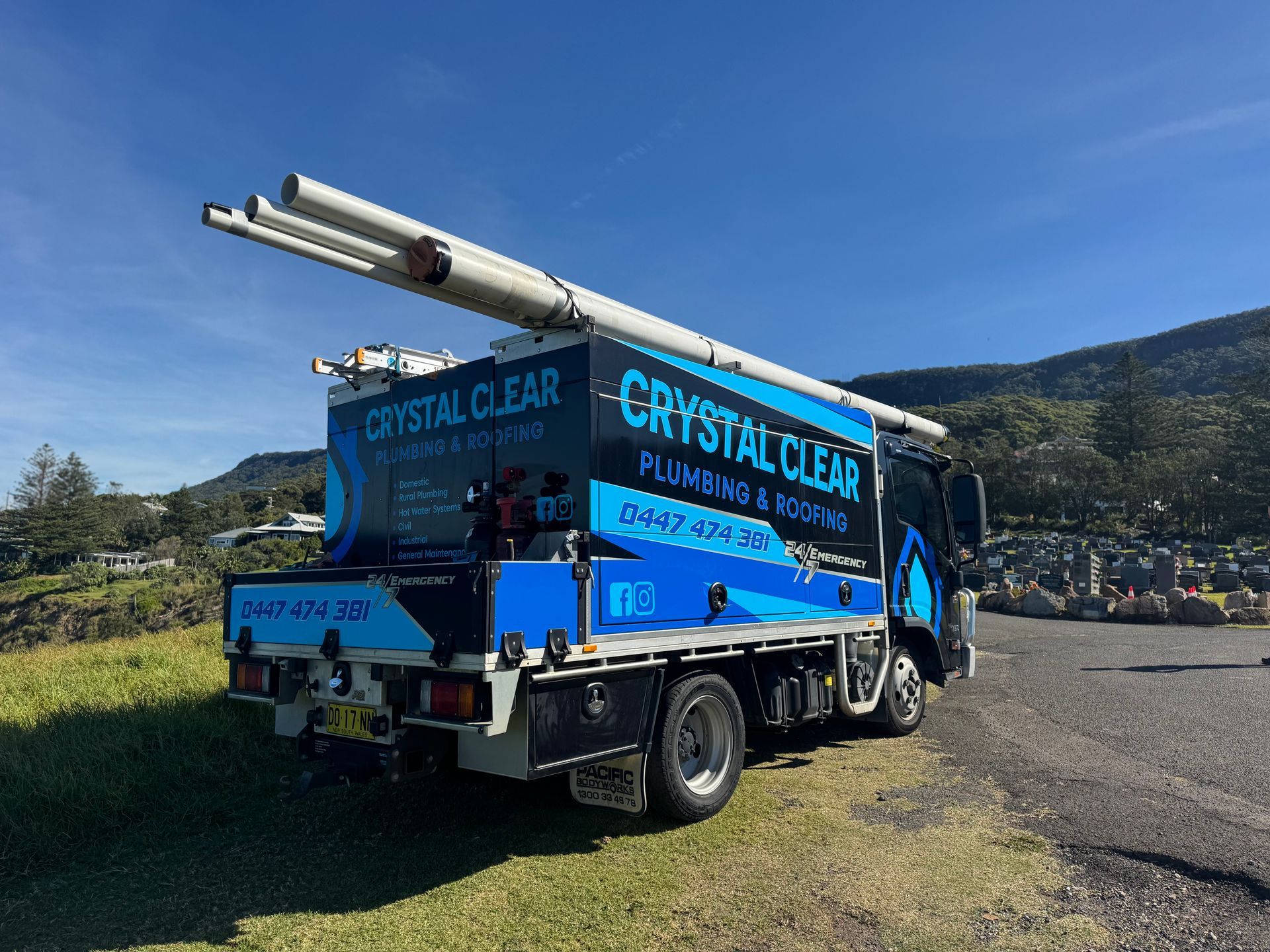 Blue Crystal Clear service truck parked on grass beside a road with mountains in the background — Crystal Clear Plumbing & Roofing in Wollongong, NSW